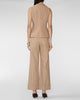 A model shown from the back wearing a beige sleeveless vest and matching wide-leg trousers, paired with dark brown pointed-toe heels against a light gray studio background.