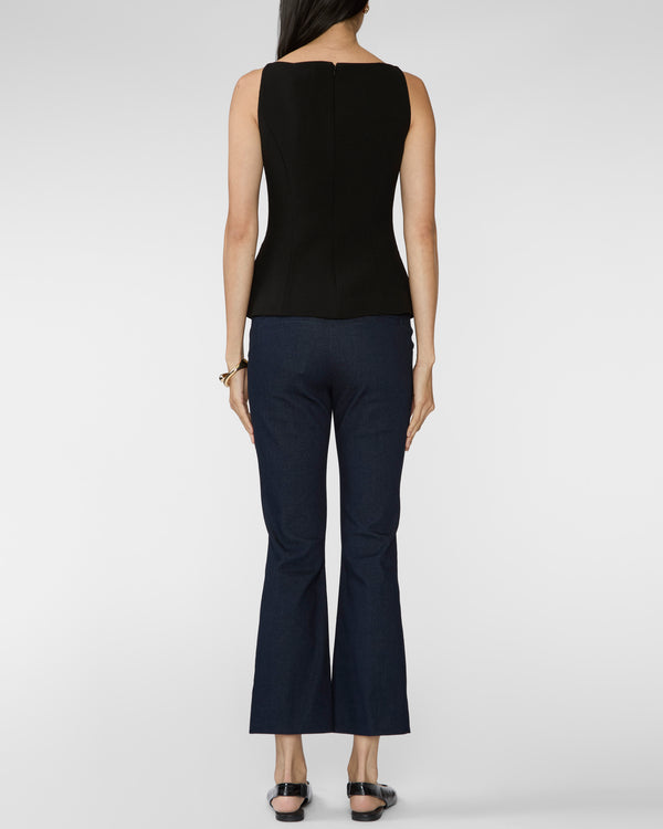 A woman shown from the back wearing a sleeveless black top and dark navy flared pants, standing against a light gray studio background.