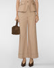 A model wearing a beige cropped blazer and matching wide-leg cropped trousers, holding a brown handbag, against a light gray studio background.