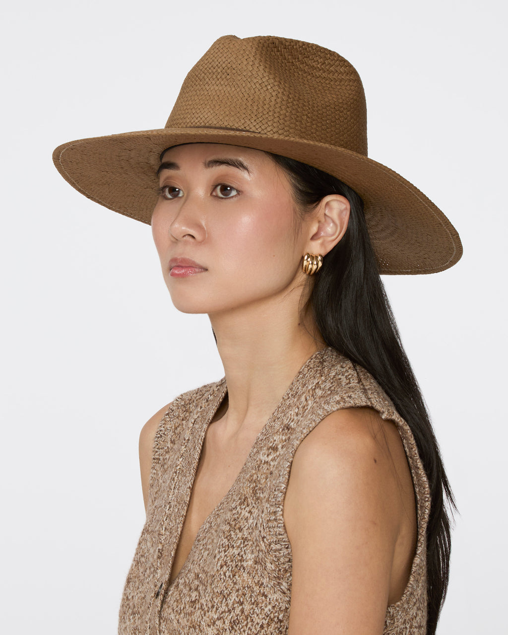 A woman wearing a brown woven wide-brim hat and a textured sleeveless top, shown in profile against a light gray studio background.
