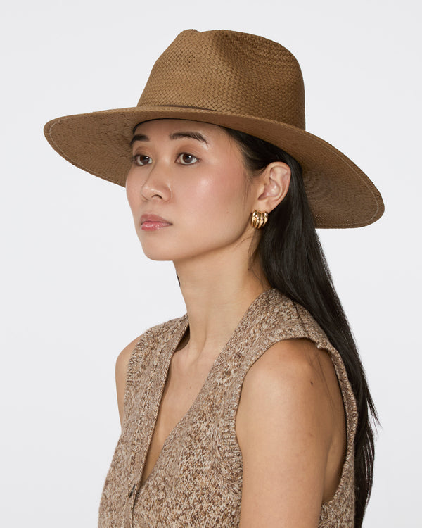 A woman wearing a brown woven wide-brim hat and a textured sleeveless top, shown in profile against a light gray studio background.