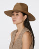 A woman wearing a brown woven wide-brim hat and a textured sleeveless top, shown in profile against a light gray studio background.