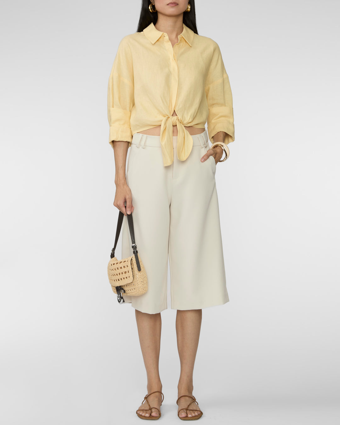 Woman wearing a yellow shirt and white skirt with a beige bag on a white background