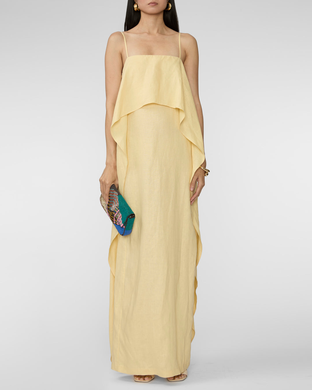Woman wearing a yellow dress holding a clutch against a white background